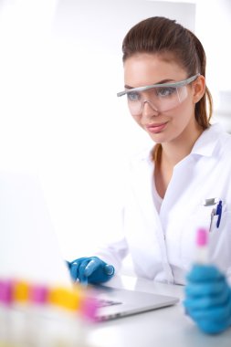 Kadın araştırmacı, beyaz arka planda izole edilmiş ilaç şişeleri ve mataralarla çevrili.