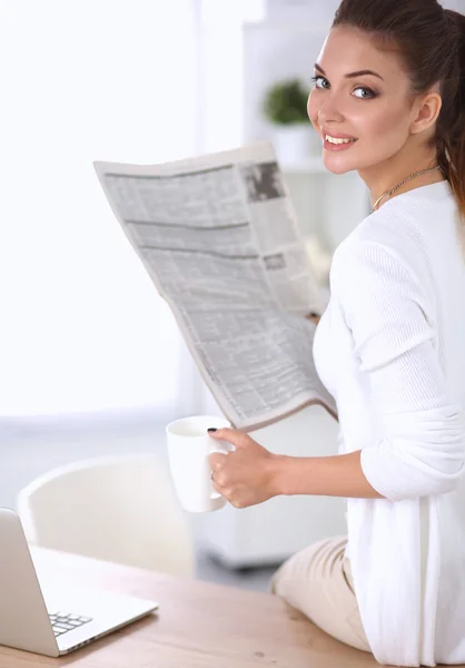 Cute businesswoman holding newspaper sitting at her desk in bright office