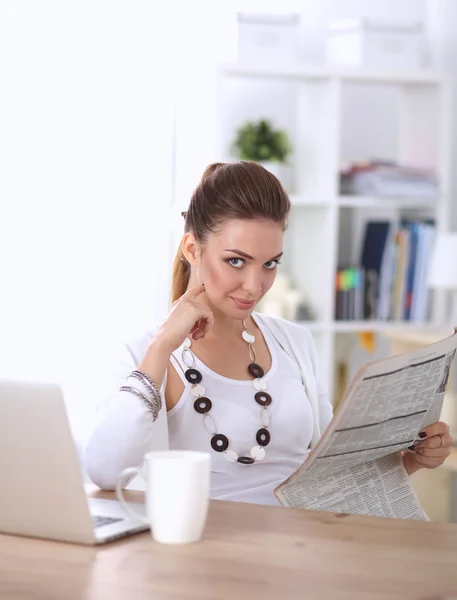Cute businesswoman holding newspaper sitting at her desk in bright office — Stock Photo, Image