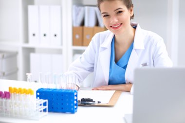 Kadın araştırmacı, beyaz arka planda izole edilmiş ilaç şişeleri ve mataralarla çevrili.