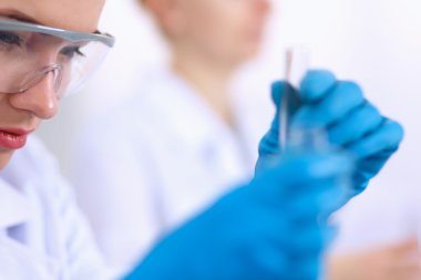 Kadın araştırmacı, beyaz arka planda izole edilmiş ilaç şişeleri ve mataralarla çevrili.