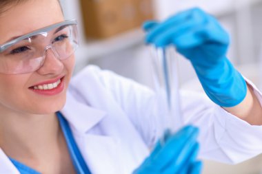 Kadın araştırmacı, beyaz arka planda izole edilmiş ilaç şişeleri ve mataralarla çevrili.