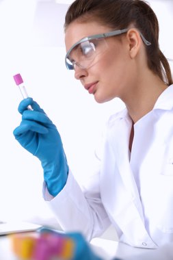 Kadın araştırmacı, beyaz arka planda izole edilmiş ilaç şişeleri ve mataralarla çevrili.