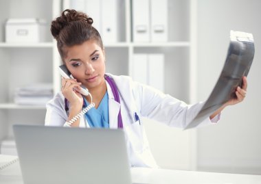 Röntgen taraması yapan kadın doktor teşhis merkezinde telefonla konuşuyor, masada oturuyor.