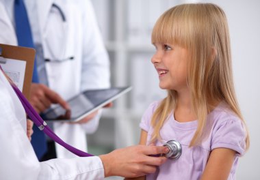 Kadın doktor ameliyatta steteskopla çocuğu muayene ediyor.