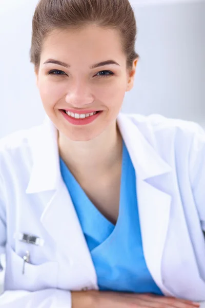 Mooie jonge glimlachende vrouwelijke arts zittend aan het bureau . — Stockfoto