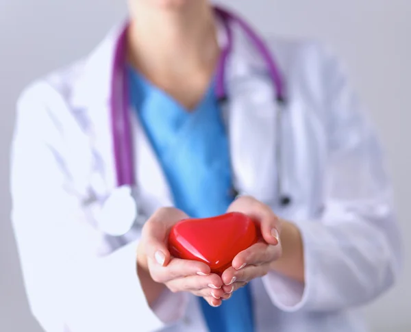 Mujer joven médico sosteniendo un corazón rojo, de pie sobre fondo gris — Foto de Stock