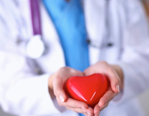 Mujer joven médico sosteniendo un corazón rojo, de pie sobre fondo gris — Foto de Stock