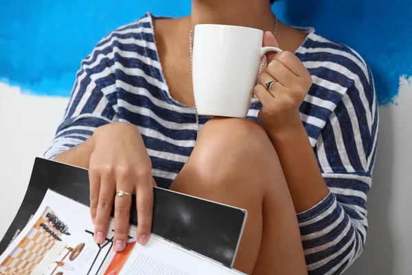 Porträtt av kvinnliga målare sitter på golvet nära väggen efter paintingand håller en kopp — Stockfoto