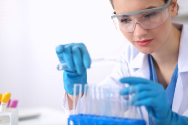 Kadın araştırmacı, beyaz arka planda izole edilmiş ilaç şişeleri ve mataralarla çevrili.