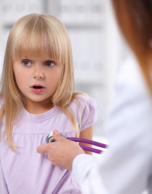 Kadın doktor ameliyatta steteskopla çocuğu muayene ediyor.