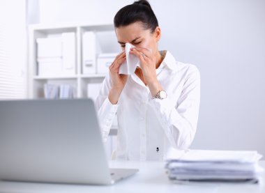 Genç iş kadını burnunu siliyor, masada oturuyor.