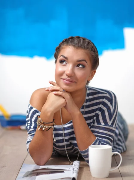 Portret van vrouwelijke schilder liggend op de vloer in de buurt van muur na paintingand holding een kop — Stockfoto