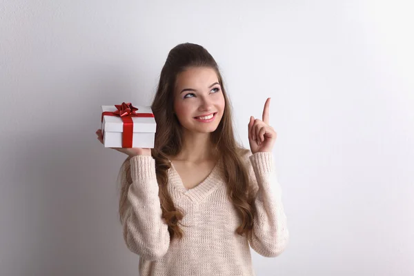 Jonge vrouw gelukkig glimlach houden de doos van de gift in handen, permanent over grijze achtergrond — Stockfoto