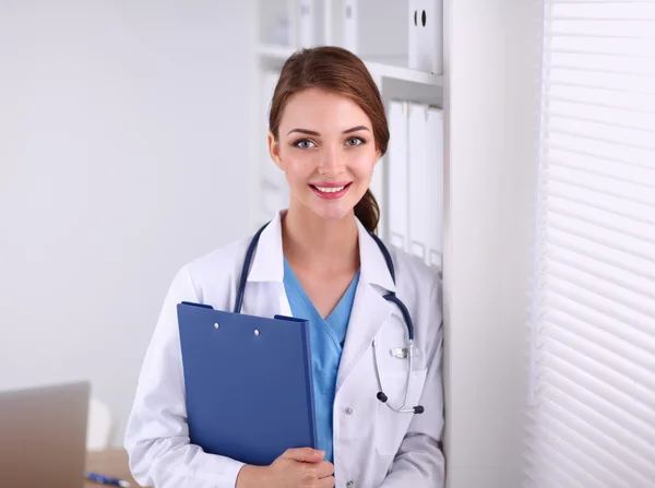 Médecin souriante avec un dossier en uniforme debout à l'hôpital — Photo