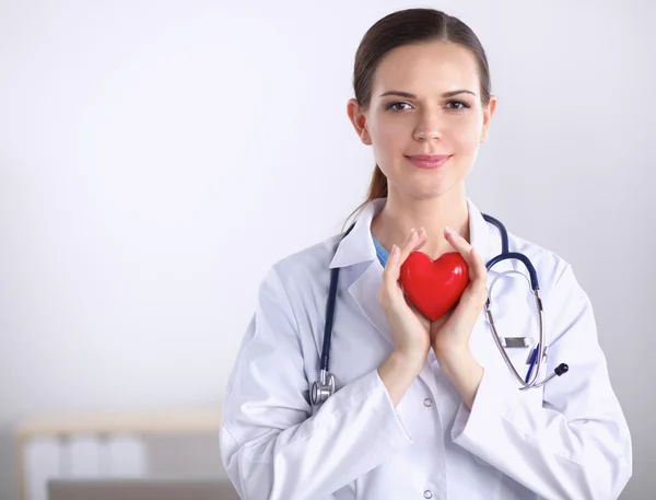 Kırmızı bir kalp taşıyan genç bir kadın doktor, beyaz arka planda izole edilmiş.
