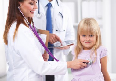 Kadın doktor ameliyatta steteskopla çocuğu muayene ediyor.