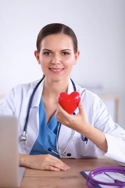 Junger Arzt mit rotem Herzsymbol sitzt am Schreibtisch — Stockfoto