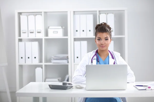 Doctora sentada en el escritorio y trabajando en un portátil — Foto de Stock