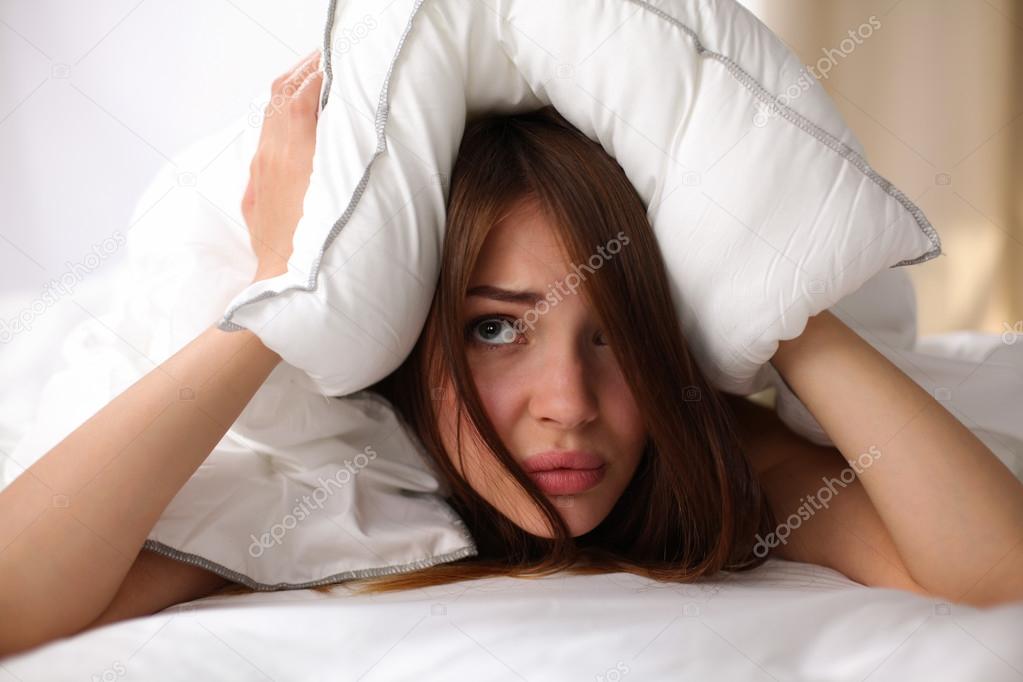 Female lying on bed and closing her ears with pillow