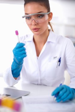 Kadın araştırmacı, beyaz arka planda izole edilmiş ilaç şişeleri ve mataralarla çevrili.