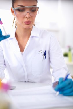 Kadın araştırmacı, beyaz arka planda izole edilmiş ilaç şişeleri ve mataralarla çevrili.