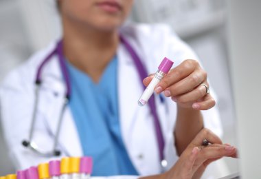 Kadın araştırmacı, beyaz arka planda izole edilmiş ilaç şişeleri ve mataralarla çevrili.