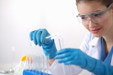 Kadın araştırmacı, beyaz arka planda izole edilmiş ilaç şişeleri ve mataralarla çevrili.