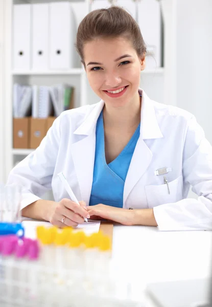Hermosa joven sonriente doctora sentada en el escritorio . —  Fotos de Stock