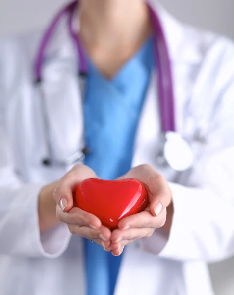 Mujer joven médico sosteniendo un corazón rojo, de pie sobre fondo gris — Foto de Stock