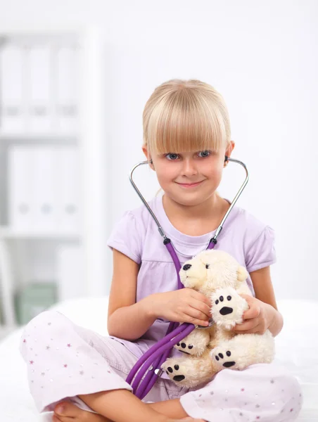 Klein meisje onderzoekt haar teddybeer met stethoscoop. — Stockfoto