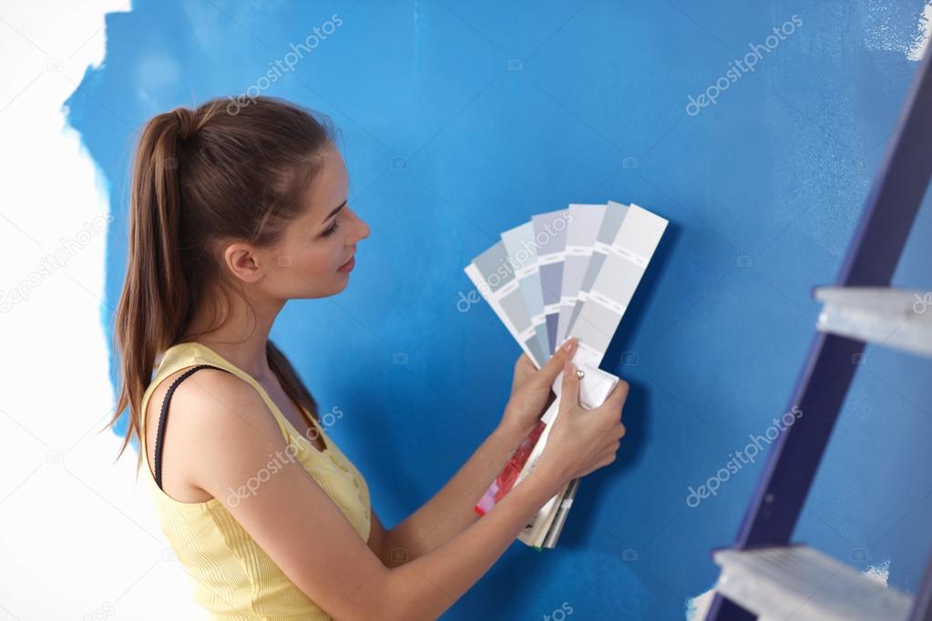 Young beautiful woman holding color palette , standing near wall.