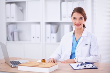 Güzel, genç, gülümseyen bayan doktor masada oturuyor ve yazıyor..