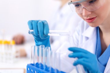 Kadın araştırmacı, beyaz arka planda izole edilmiş ilaç şişeleri ve mataralarla çevrili.