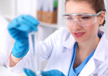 Kadın araştırmacı, beyaz arka planda izole edilmiş ilaç şişeleri ve mataralarla çevrili.