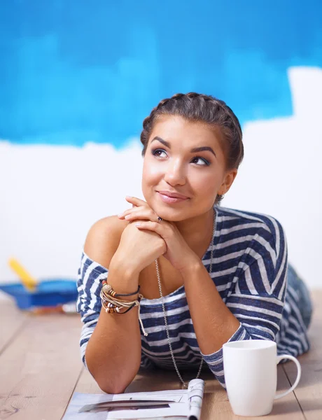 Retrato de pintora tendida en el suelo cerca de la pared después de pintar y sostener una taza — Foto de Stock