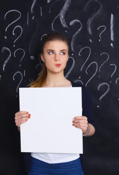 Young girl with question mark holding a blank on  gray background — Stock Photo, Image
