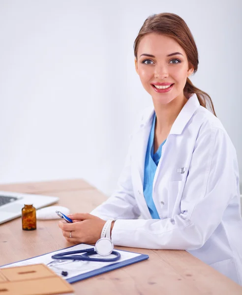 Красивая молодая улыбающаяся женщина-врач сидит за столом и пишет:. — стоковое фото