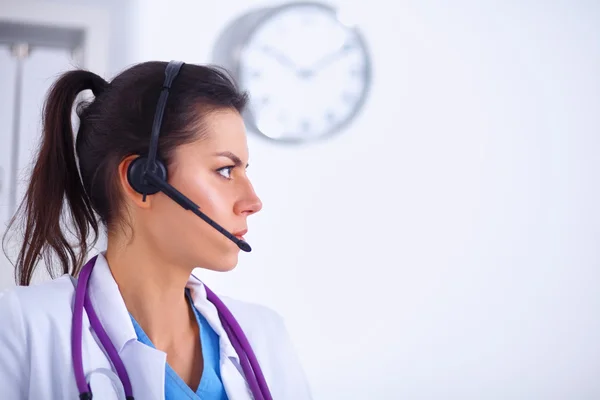 Médico usando fone de ouvido sentado atrás de uma mesa com laptop — Fotografia de Stock