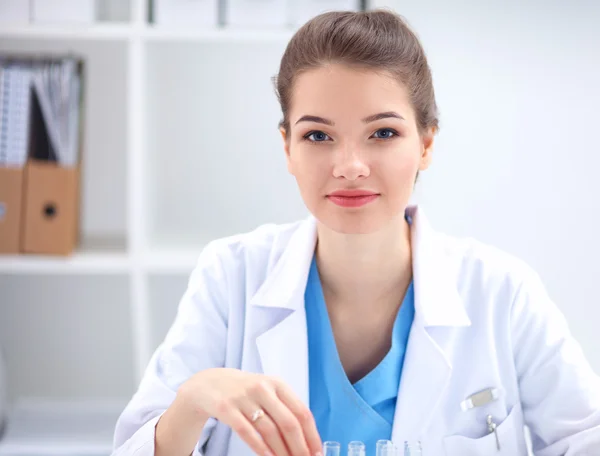 Vacker ung leende kvinnlig läkare sitter vid skrivbordet . — Stockfoto