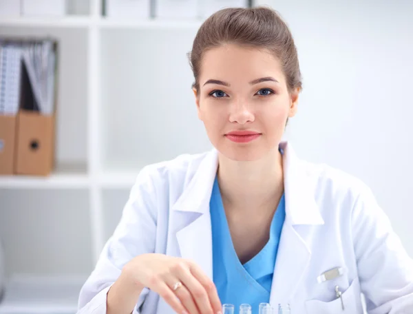 Hermosa joven sonriente doctora sentada en el escritorio . —  Fotos de Stock