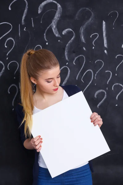 Young girl with question mark holding a blank on  gray background — Stock Photo, Image