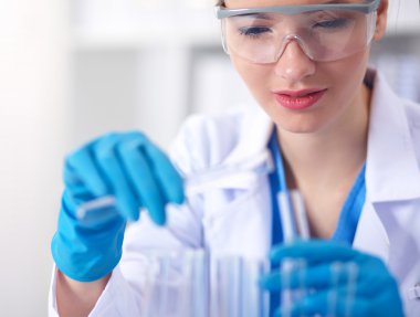 Kadın araştırmacı, beyaz arka planda izole edilmiş ilaç şişeleri ve mataralarla çevrili.