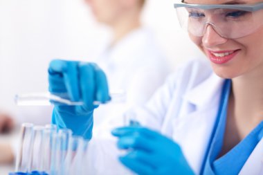 Kadın araştırmacı, beyaz arka planda izole edilmiş ilaç şişeleri ve mataralarla çevrili.