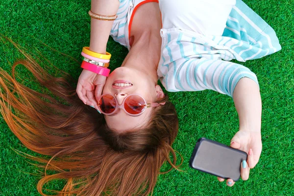 Mooie jonge vrouw selfie maken door haar telefoon liggend in groene gras — Stockfoto