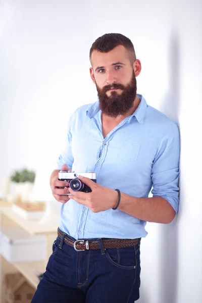 Homem barba jovem segurando uma câmera enquanto de pé contra o fundo branco — Fotografia de Stock