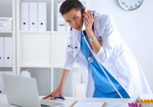 Jovem médico mulher em casaco branco no computador usando telefone — Fotografia de Stock