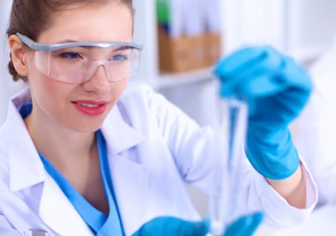 Kadın araştırmacı, beyaz arka planda izole edilmiş ilaç şişeleri ve mataralarla çevrili.