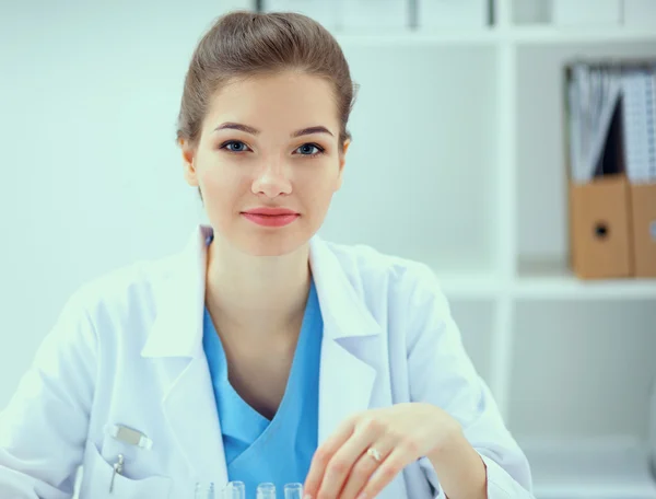 Vacker ung leende kvinnlig läkare sitter vid skrivbordet . — Stockfoto