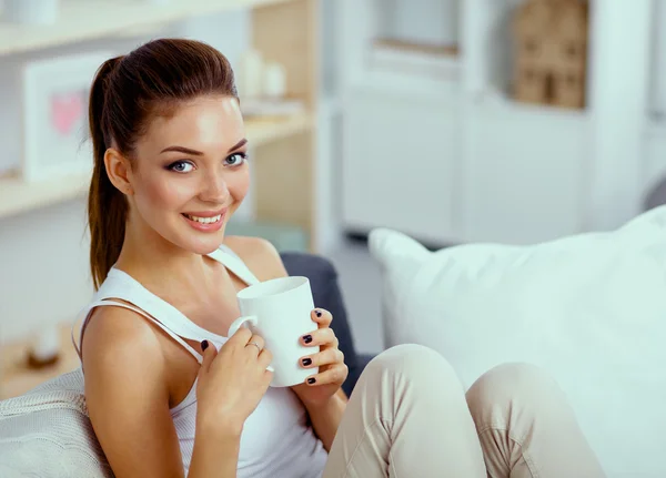 Giovane bella donna con una tazza sul divano a casa — Foto Stock